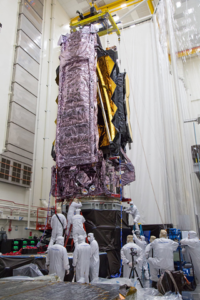 NASA scientists perform environmental testing on the James Webb Space Telescope. Several scientists in protective gear surround the in development telescope.