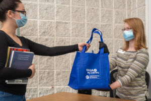 Woman holding books handing another woman a bag filled with activity materials