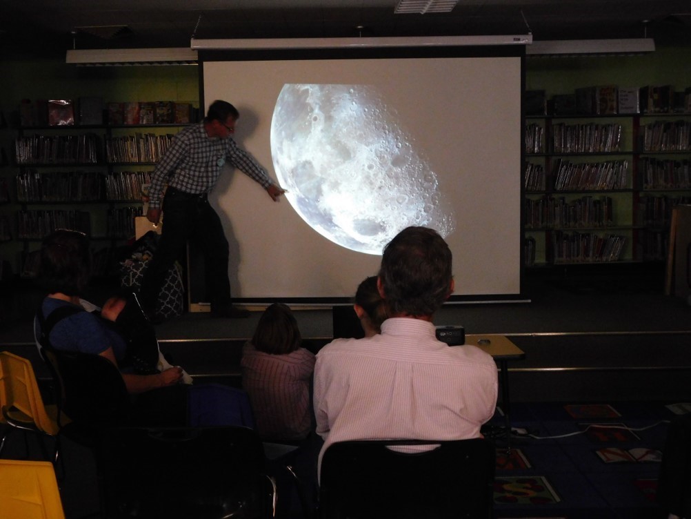Man points to image of the Moon on a projector screen in front of an audience