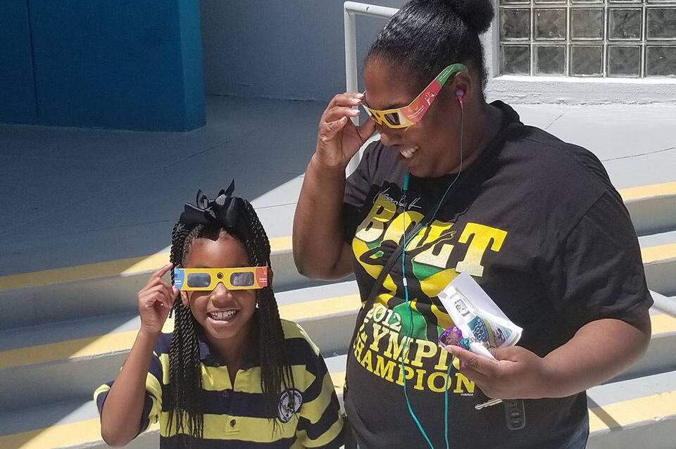 Child wearing solar eclipse glasses and adult with solar eclipse glasses